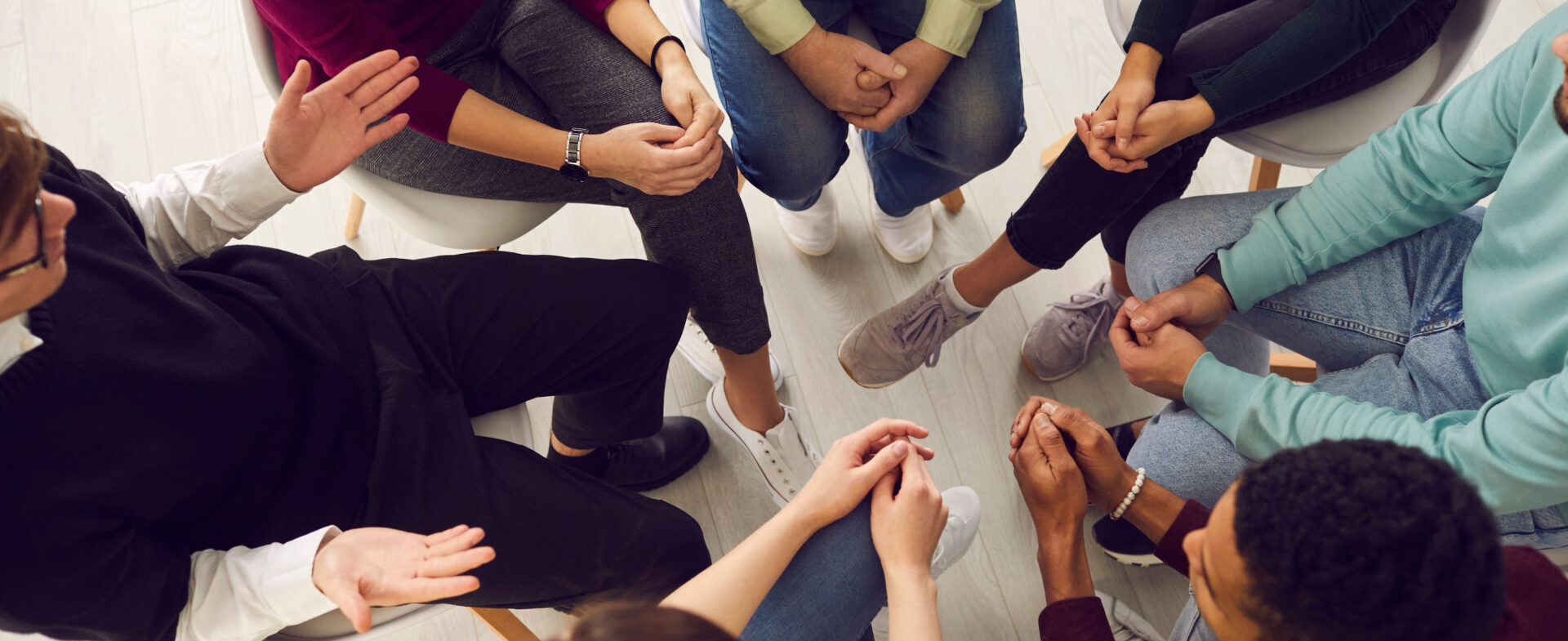 Top view of diverse people sitting in a close circle and talking to a therapist. Cropped image of unidentified people receive help and support during a group therapy session. Concept of group therapy. - behavioral health services dallas