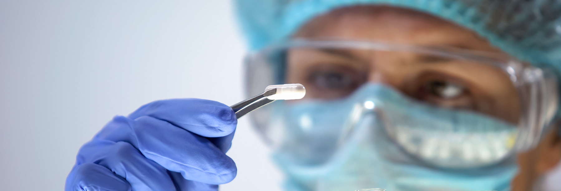 a female researcher in a protective cap, eyewear and latex gloves holding a pill capsule with tweezers and examining it closely - clinical research trials dallas hiv