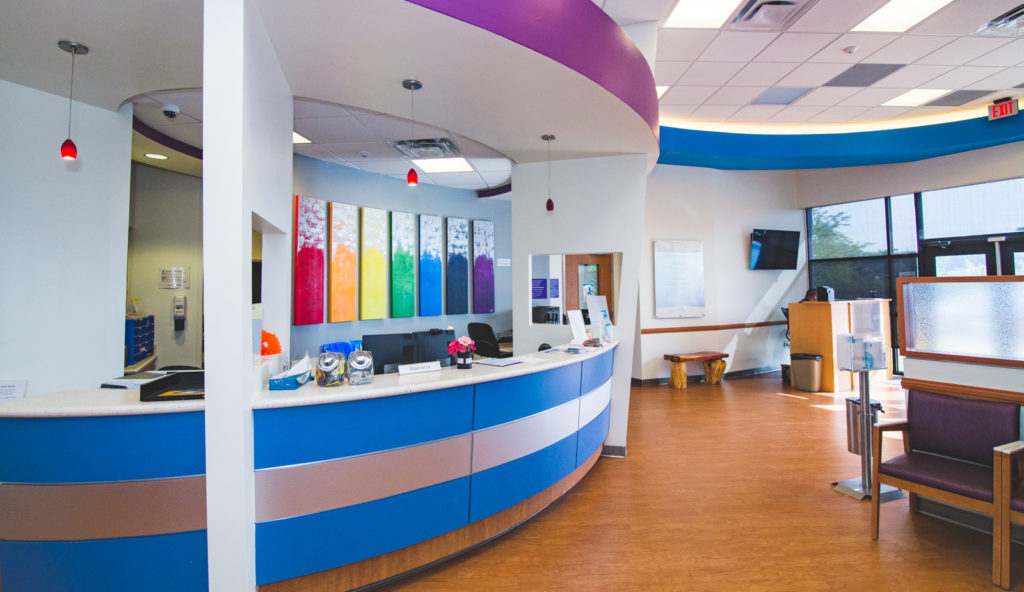 shot of lobby of PHNTX South Dallas Health Center with waist high counter and spectrum 6 panel art on the wall