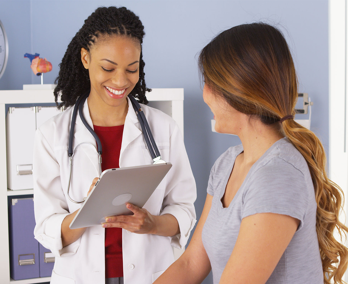 Black female provider with tablet talking to Asian female patient
