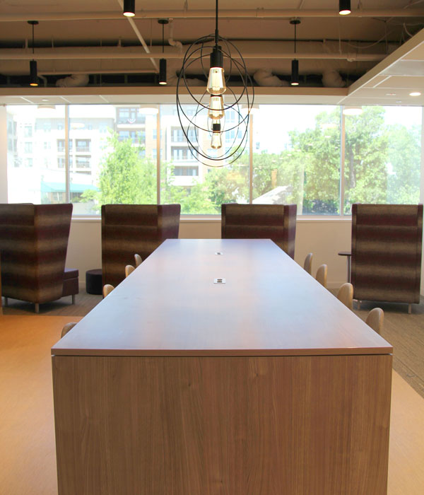 Long rectangle wood table in middle of image pointing toward four high wing back chairs facing a wall of windows