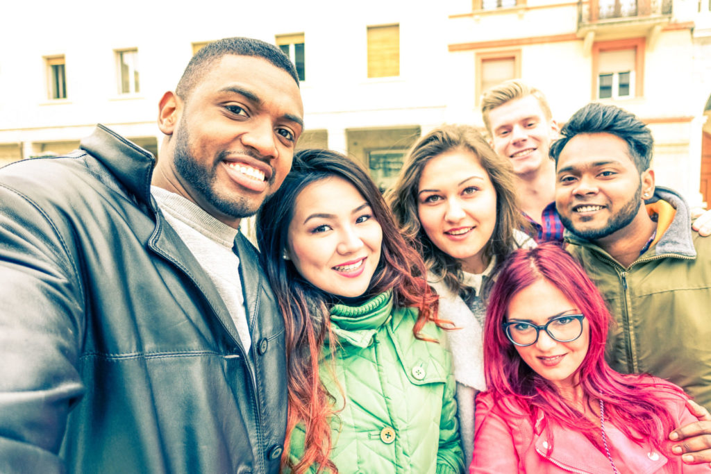 Multiracial group of friends taking selfie standing on the street at winter season - Happy students smiling at phone camera in a joyful self portrait - Concept of teenage cheerful moments together