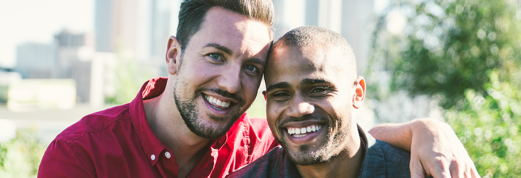 interracial gay couple smiling and hugging outdoors