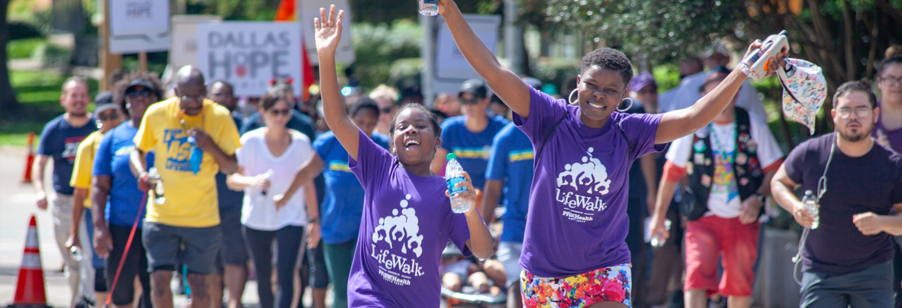 Black mother and daughter walking with hands in the air in front during LifeWalk with people walking behind them