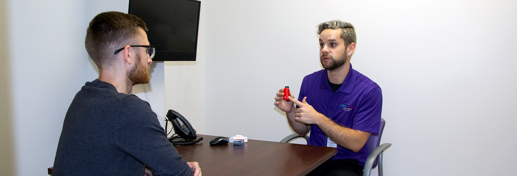 White male pharmacist sitting across and explaining a medication to a white male patient