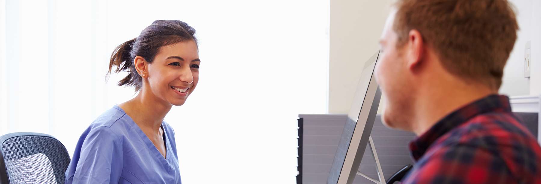 female nurse sitting in front of a computer with white male patient