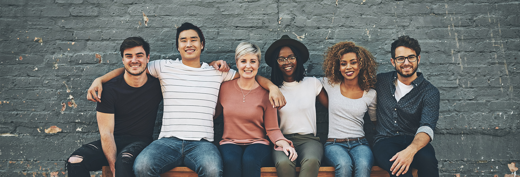 Group of diverse friends sitting on a bench against a brick wall