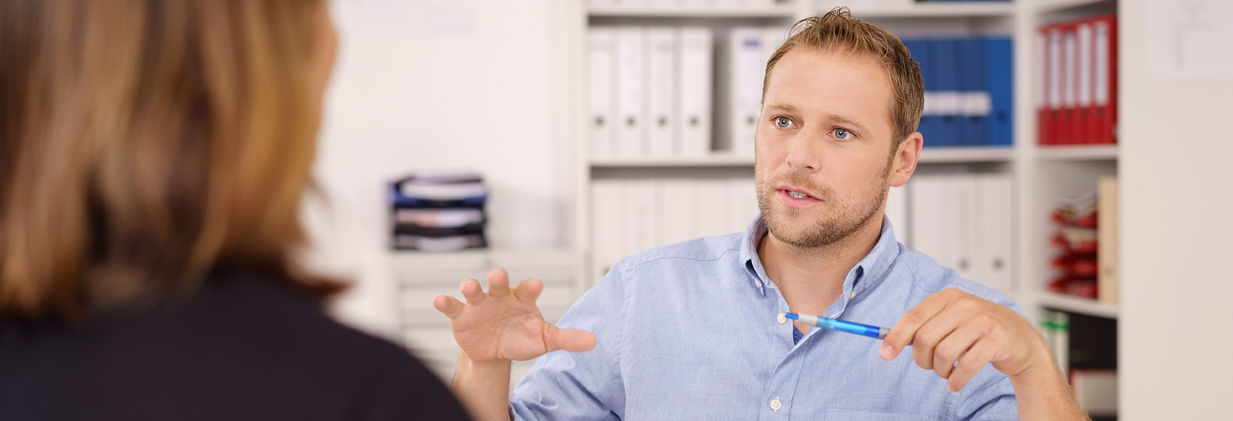 white male talking with hands across a female in an office