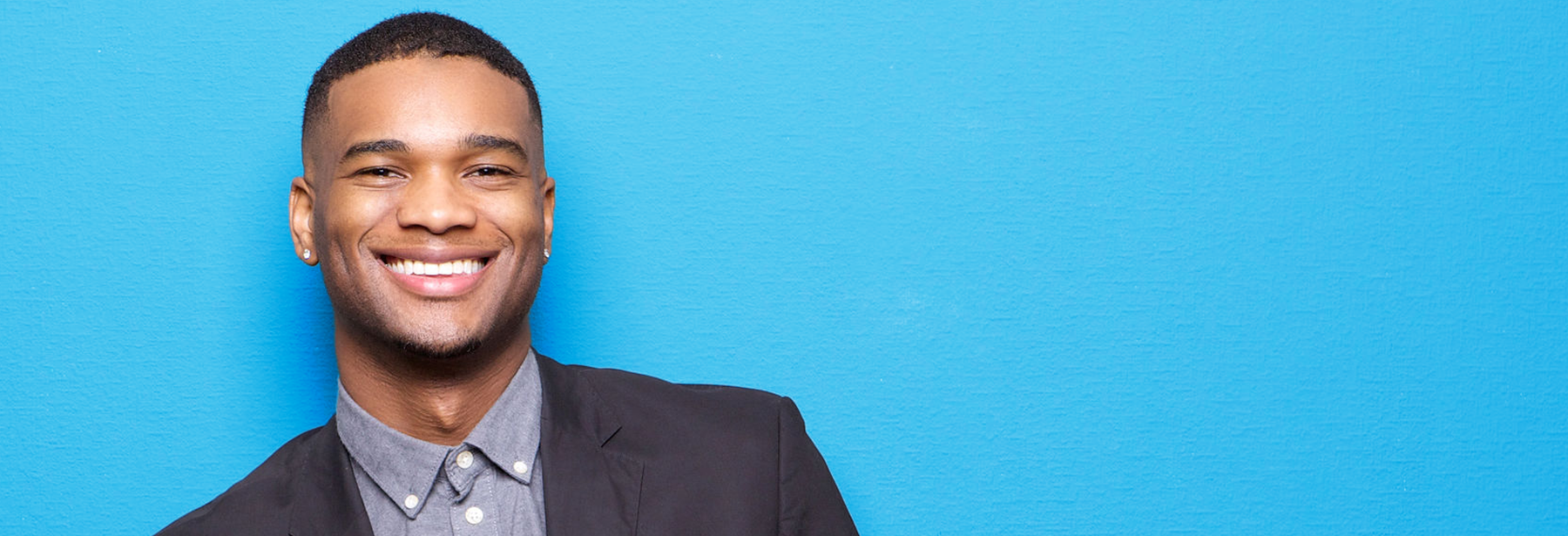 young smiling black male wearing a suit in front of a blue background