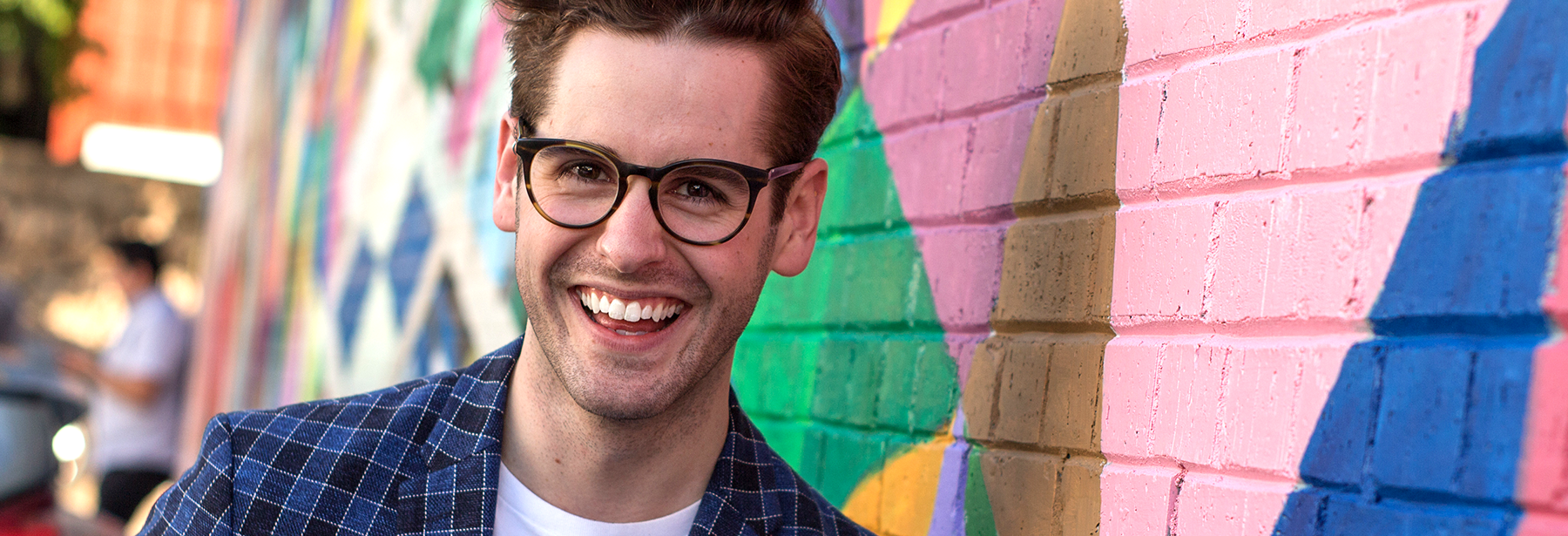 young white male smiling in front of a colorful mural outdoors