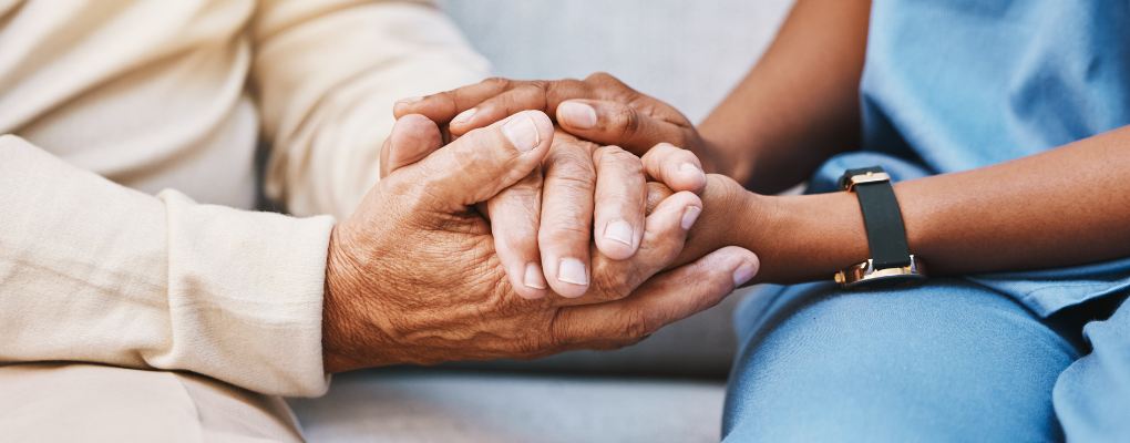 Black nurse holding hands with a Caucasian patient