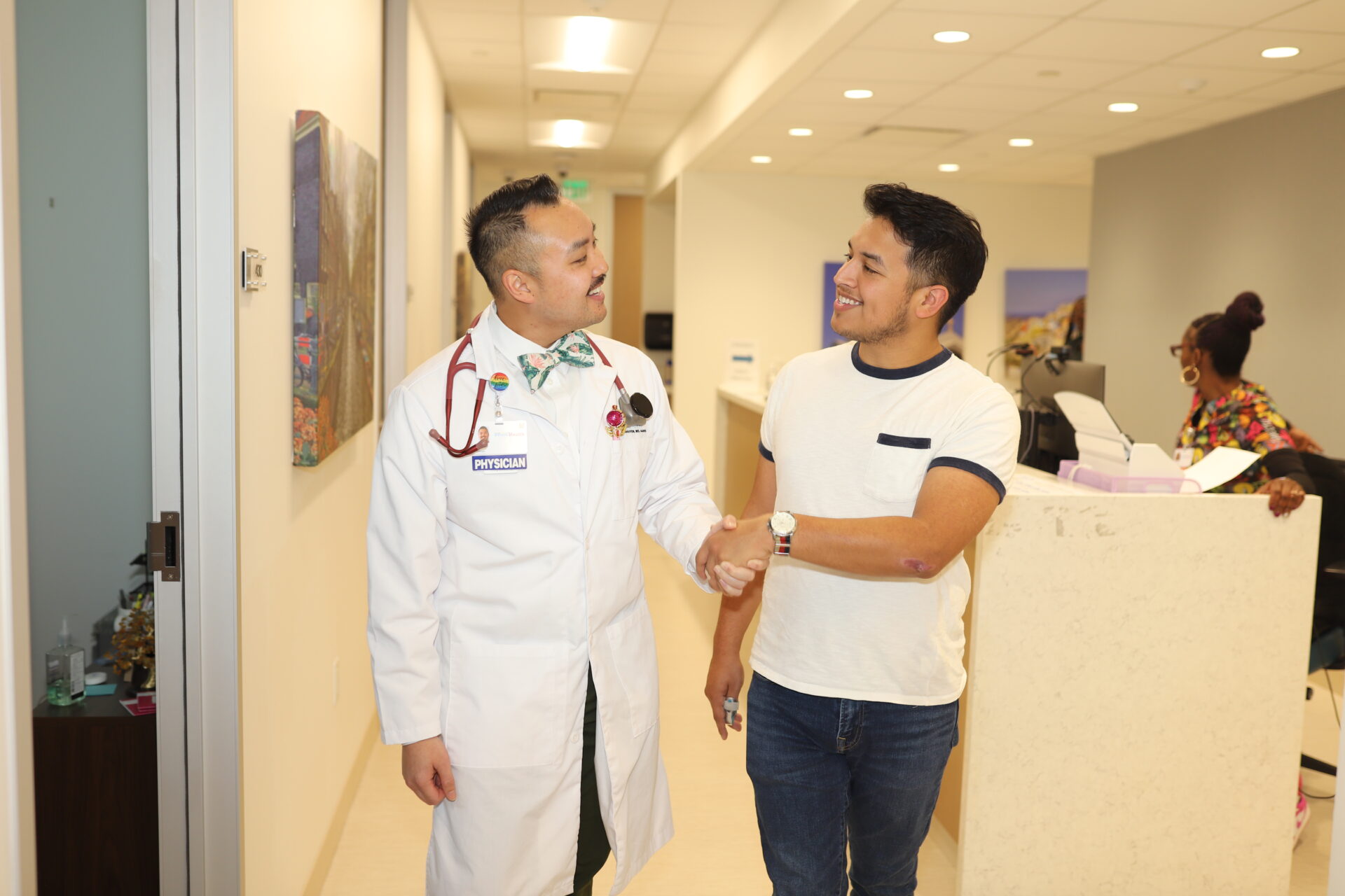 A photo of Dr. Nguyen shaking a patient's hand as they walk toward the waiting room together at PHNTX South Dallas Health Center. A medical assistant can be seen in the background.