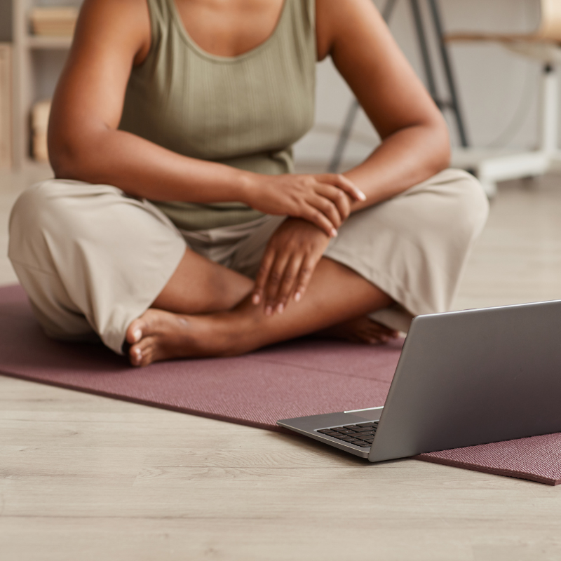 a curvy woman sitting on a yoga mat with her laptop open, possibly about to start a yoga video online - healthy family habits