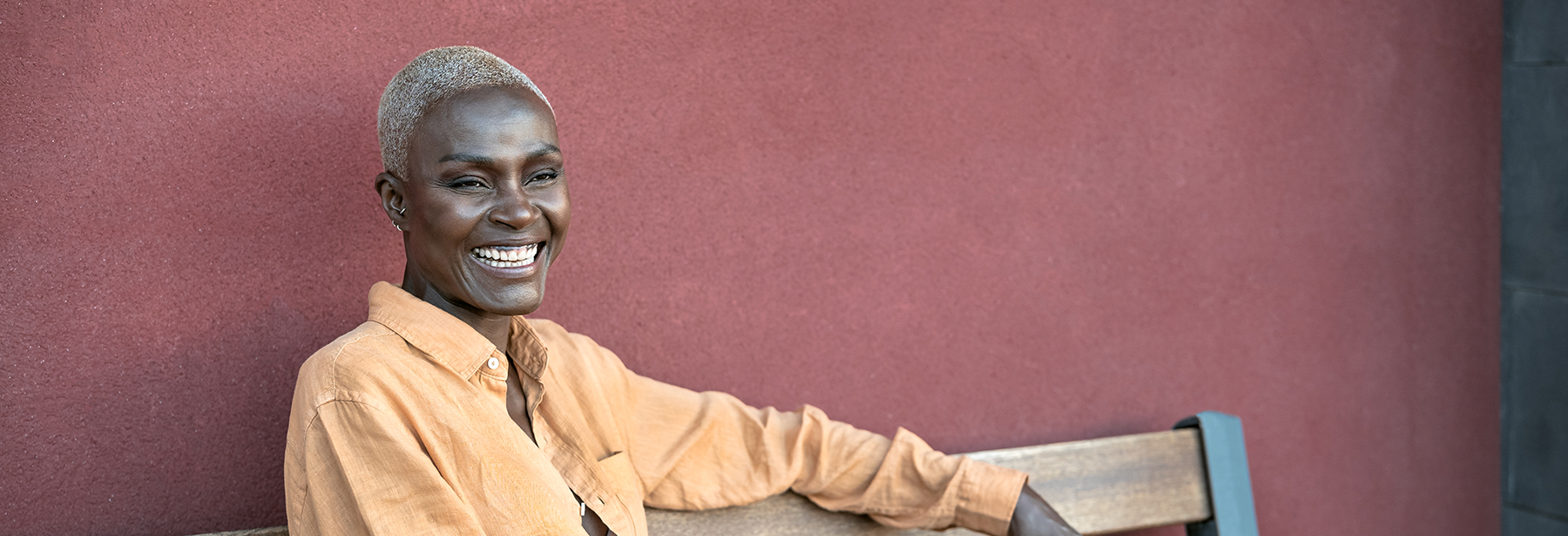 Black woman in an orange blouse sitting on a bench smiling.